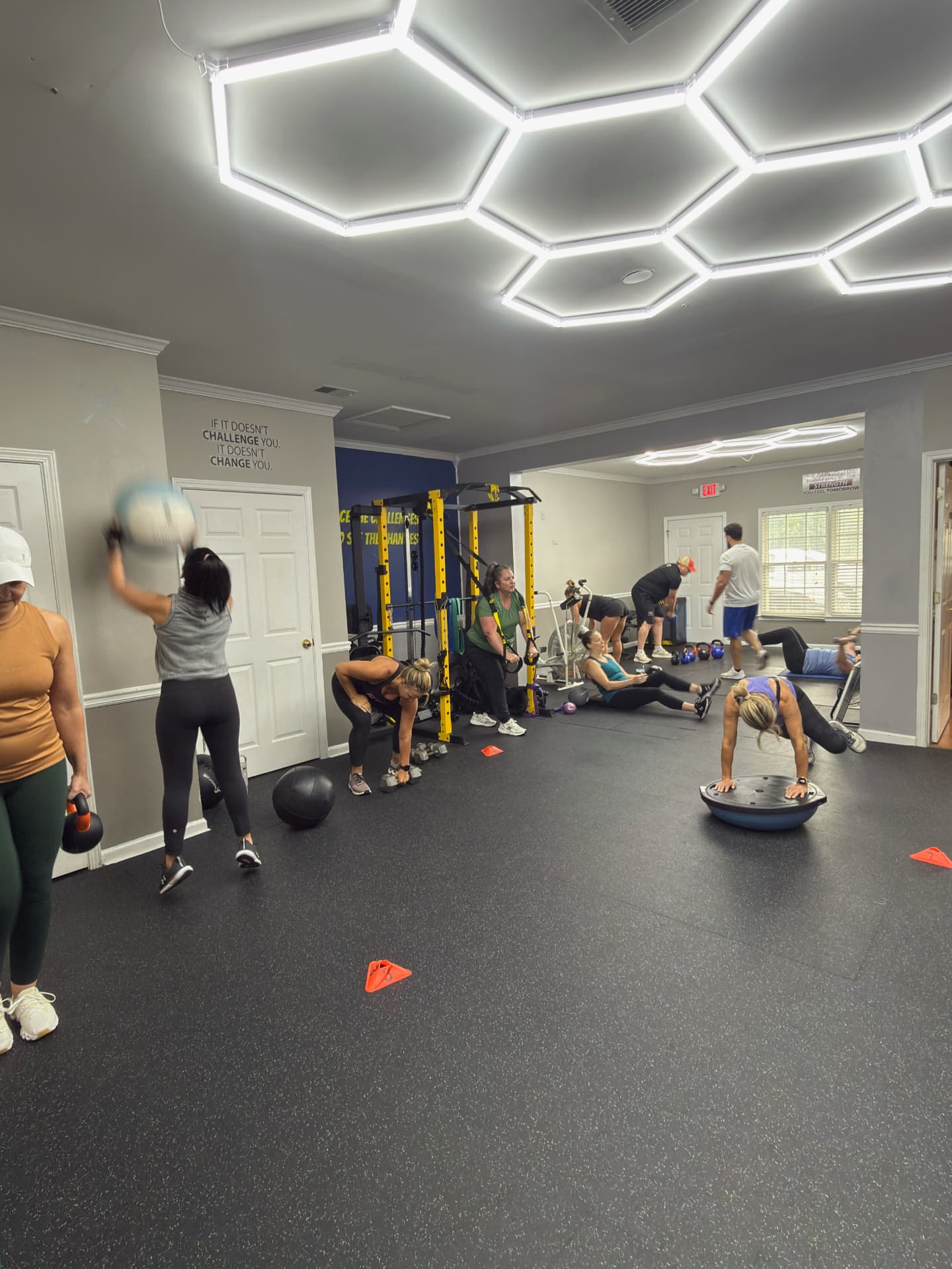 Members training with kettlebells, dumbbells and a BOSU under hexagon lights on the floor at Hive Fitness Journey, a gym in Woodstock GA